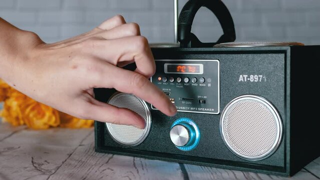 Female Hands Pressing Buttons, Rotates Handle on a Portable Audio Tape Recorder. Volume, play, mode. Player, radio with two stereo speakers with USB input against the background of flowers on desk.