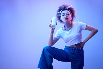 Young positive kazakh girl with afro hairstyle listens music in portable speaker, dances and poses,...