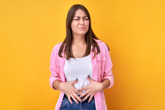 Brunette woman puts hands on stomach feels pain, medical or gynecological health problems isolated on yellow background