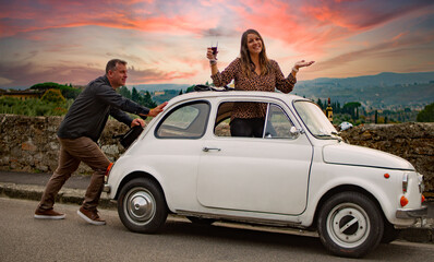 Husband pushing wife drinking wine in Fiat in Italy Wine Country 