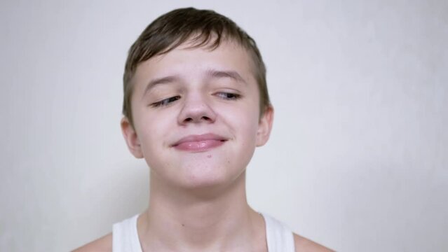 A Smiling Boy with Lowered Eyelids Rotates his Eyes in Different Directions. Tricky glance. Smirk. Myopia. Ptosis. Eye rotation. Strabismus. Syndrome. Facial nerve problem. Bad vision concept. Humor.