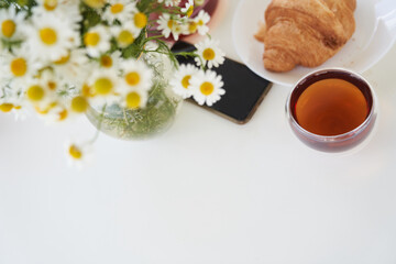 Top view of a tea with fresh sweet croissants on the table with a vase of daisies. In the middle of the table is a smartphone. Sunday breakfast in backyard of a cottage. Copy space. High quality photo