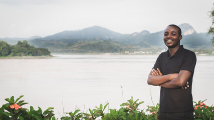 Fototapeta premium Smile African man standing by a river with a mountain background..Concept of rural people and rivers