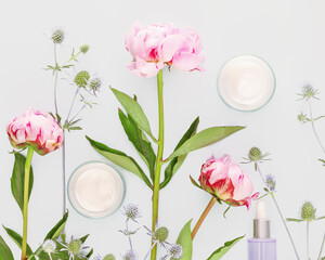 Glass cosmetic jars with cream, serum and beautiful, pink peonies on a blue background. Natural, flower beauty products. Organic, moisturizing, beauty care products