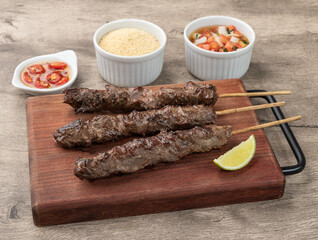 Meat skewers over wooden board with farofa and vinaigrette