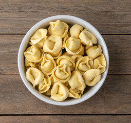 Uncooked cappelletti or tortellini on a bowl over wooden table
