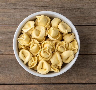 Uncooked cappelletti or tortellini on a bowl over wooden table