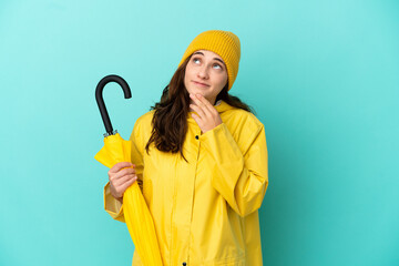 Young caucasian man holding an umbrella isolated on blue background looking up while smiling