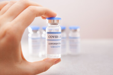 Coronavirus vaccine ampoule in woman hand on light background - vaccination medical concept