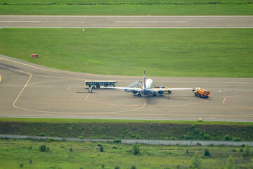 Fototapeta na wymiar rear view of a passenger plane in the parking lot next to a fuel tanker and a bus with passengers, a ramp and service personnel in green vests