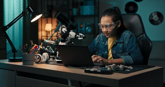 Girl fascinated by electronics watches robot, plays with toy. The room at night, illuminated by a blue glow in the evening.