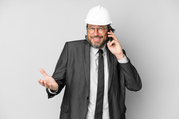 Young architect man with helmet over isolated background keeping a conversation with the mobile phone with someone