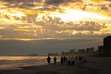 People walk on the beach under dramatic sky