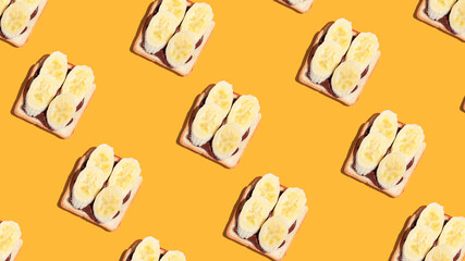 Pattern of toasted bread with banana and chocolate on yellow background.