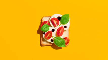 Toast with tomatoes, mozzarella cheese and basil on yellow background.