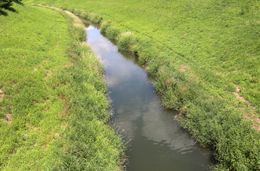 Fototapeta na wymiar Narrow river flows between grass covered banks.