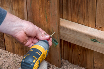 Close up of a carpenter using a power drill to screw in a fence board.