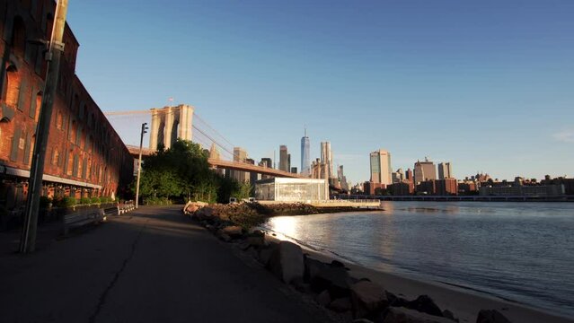 POV view. Riding by bicycle along the East river to the ferry pier. Brooklyn bridge is seen behind the trees, skyscrapers on the background. New York. Nice summer morning. 