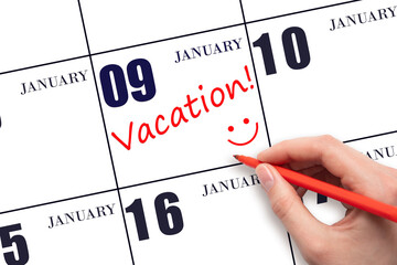 A hand writing a VACATION text and drawing a smiling face on a calendar date 9 January. Vacation...