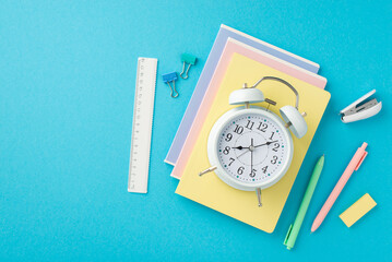 Back to school concept. Top view photo of alarm clock over stack of notebooks stapler pens eraser...