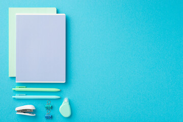 Back to school concept. Top view photo of ordered stationery composition two note pads binder clips pens stapler and round correction tape on isolated blue background with empty space