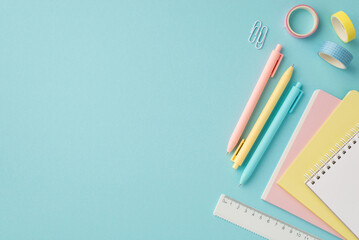 Back to school concept. Top view photo of school supplies stack of copybooks pens adhesive tape ruler and clips on isolated pastel blue background with empty space