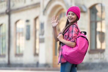 Happy teen girl back-to-school waving hand making hello or goodbye outdoors, copy space