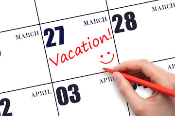 A hand writing a VACATION text and drawing a smiling face on a calendar date 27 March. Vacation...