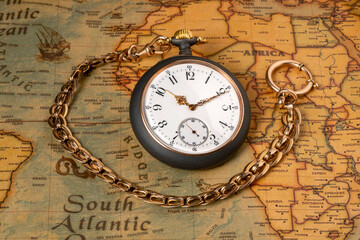 Vintage silver watch with gold chain lying on an old paper map. Round gray vintage clock with golden hands on yellow world map. Concept of travel, time, adventure. Geography, countries and continents.