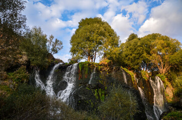 Scenic autumn landscape with High rocky waterfall Shaki flowing between large green trees and mossy rocks. Famous natural tourist attraction in Armenia.