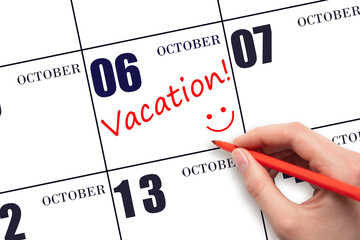 A hand writing a VACATION text and drawing a smiling face on a calendar date 6 October. Vacation planning concept.