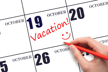 A hand writing a VACATION text and drawing a smiling face on a calendar date 19 October. Vacation...