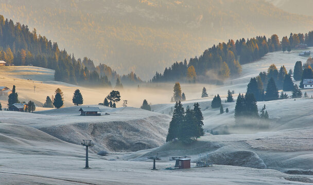 Beautiful view of traditional wooden mountain chalets on scenic Alpe di Siusi with famous Langkofel mountain peaks in the background in golden morning light at sunrise, Dolomites, Italy