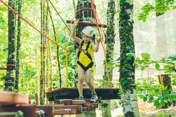 Obraz na płótnie Canvas Little girl overcomes the obstacle in the rope park. Child enjoying activity in a climbing adventure park on a summer day. 