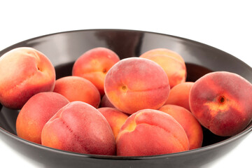Several ripe red apricots on a black ceramic plate, close-up, isolated on a white background.