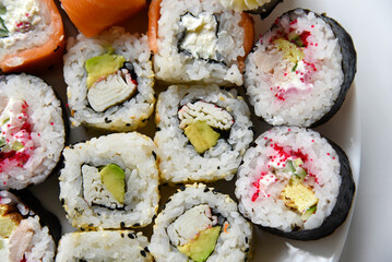 Different rice rolls with fish and cucumber on a white plate.