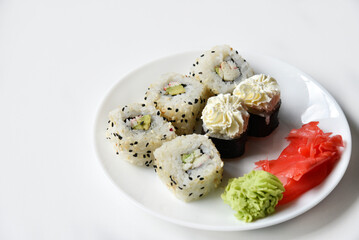 Different rice rolls with fish and cucumber on a white plate.