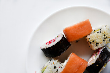 Different rice rolls with fish and cucumber on a white plate.