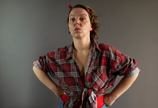 Forty-year-old pin-up woman in a plaid shirt on a gray background. Portrait of a strict woman. Adult serious pin-up woman