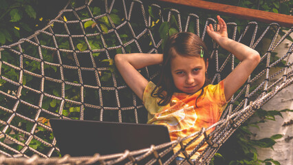 Huppy young girl working remotely with laptop outdoors in a hammock.