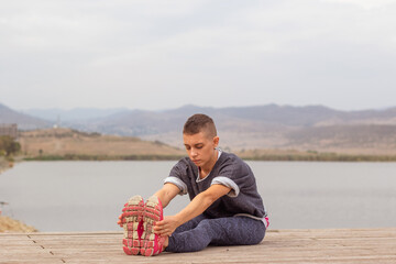 young woman with short hair doing fitness exercise on the wooden flooring near lake in mountains