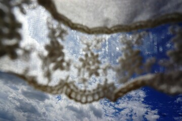 Weißer Stoff mit Spitze vor blauem Himmel mit weißen Wolken bei Sonne im Sommer