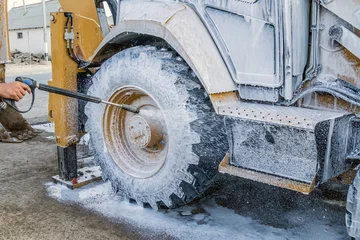Gordijnen Washing a wheeled tractor at a car wash with a foam solution © kvdkz