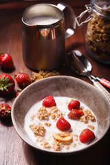 Summer breakfast with granola, fresh srawberry and milk on brown wooden table.