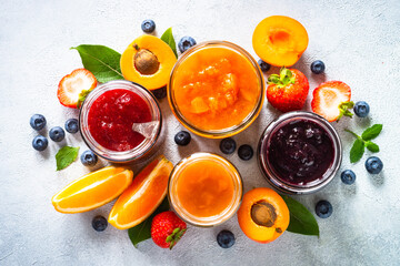 Homemade jams, natural preservation in glass jars with ingredients, fresh fruits and berries. Top view on white table.