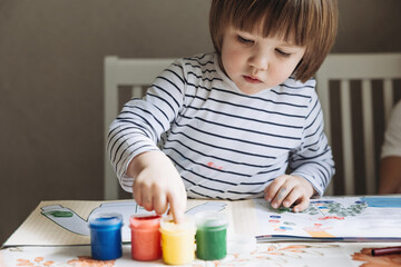Finger painting. Portrait of cute little boy painting with fingers at home. Close-up of child's...