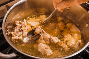 Close-up of broth and a metal spoon in a woman's hand in a steel saucepan on a stove, pieces of white chicken meat are boiled in a saucepan, top view of a hot meat broth
