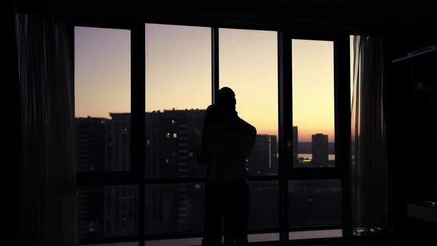 Silhouette of a guy hugging a girl against the backdrop of panoramic windows overlooking the city and sunset.