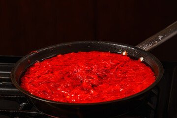 Stewed vegetables in a pan in the process of cooking Ukrainian borscht, tomatoes, red peppers, onions, carrots, beets, sugar, salt. Ukrainian national cuisine. Close-up, selective focus.