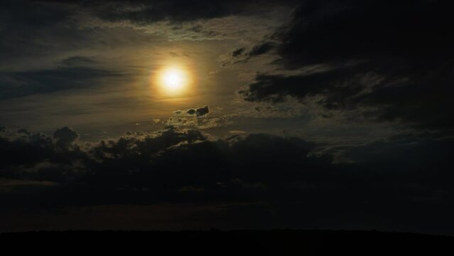 moon behind clouds above horizon at dark night, atmospheric time-lapse